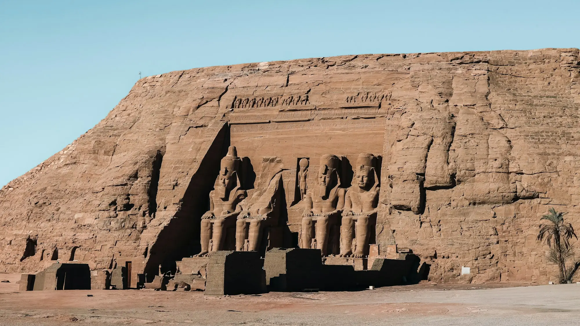 Great Temple of Abu Simbel carved into a sandstone cliff, colossal seated statues of Ramesses II, clear blue sky