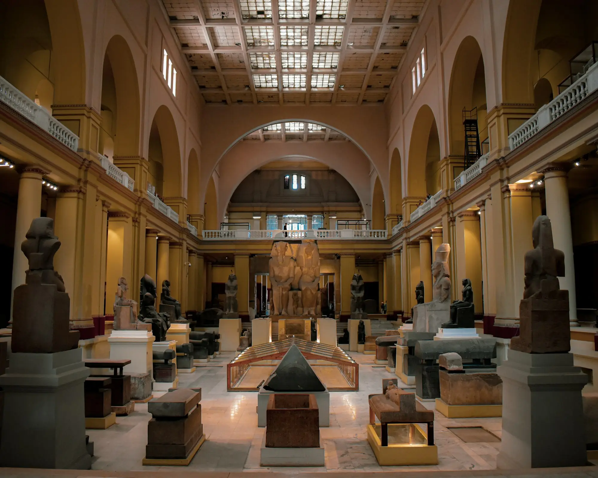 Main hall of the Egyptian Museum in Cairo lined with pharaonic statues, a pyramidion and a colossal royal pair