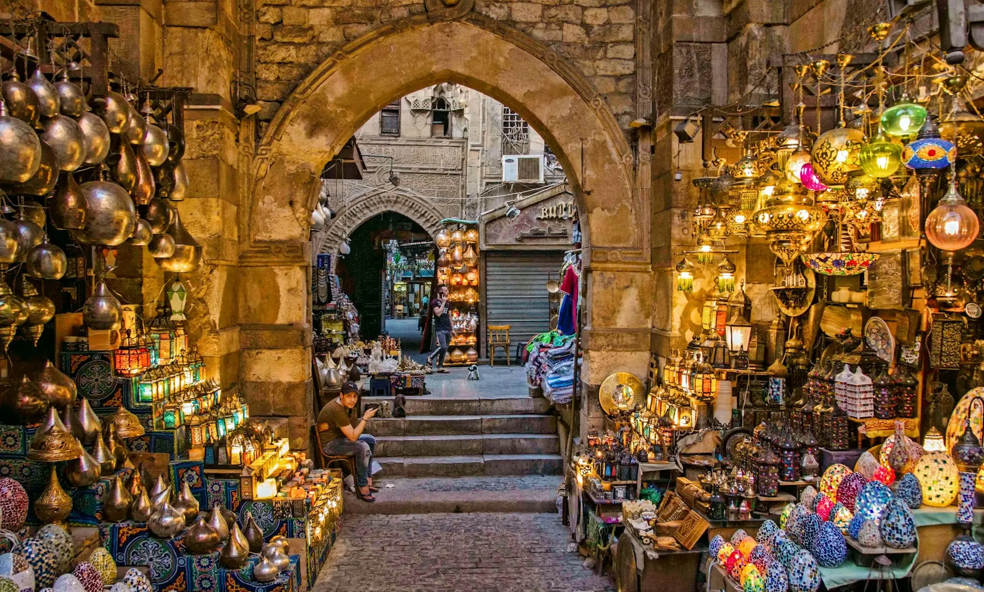 A stone archway and steps in Khan el-Khalili bazaar, flanked by shops full of glowing lanterns, brass lamps and mosaic lights