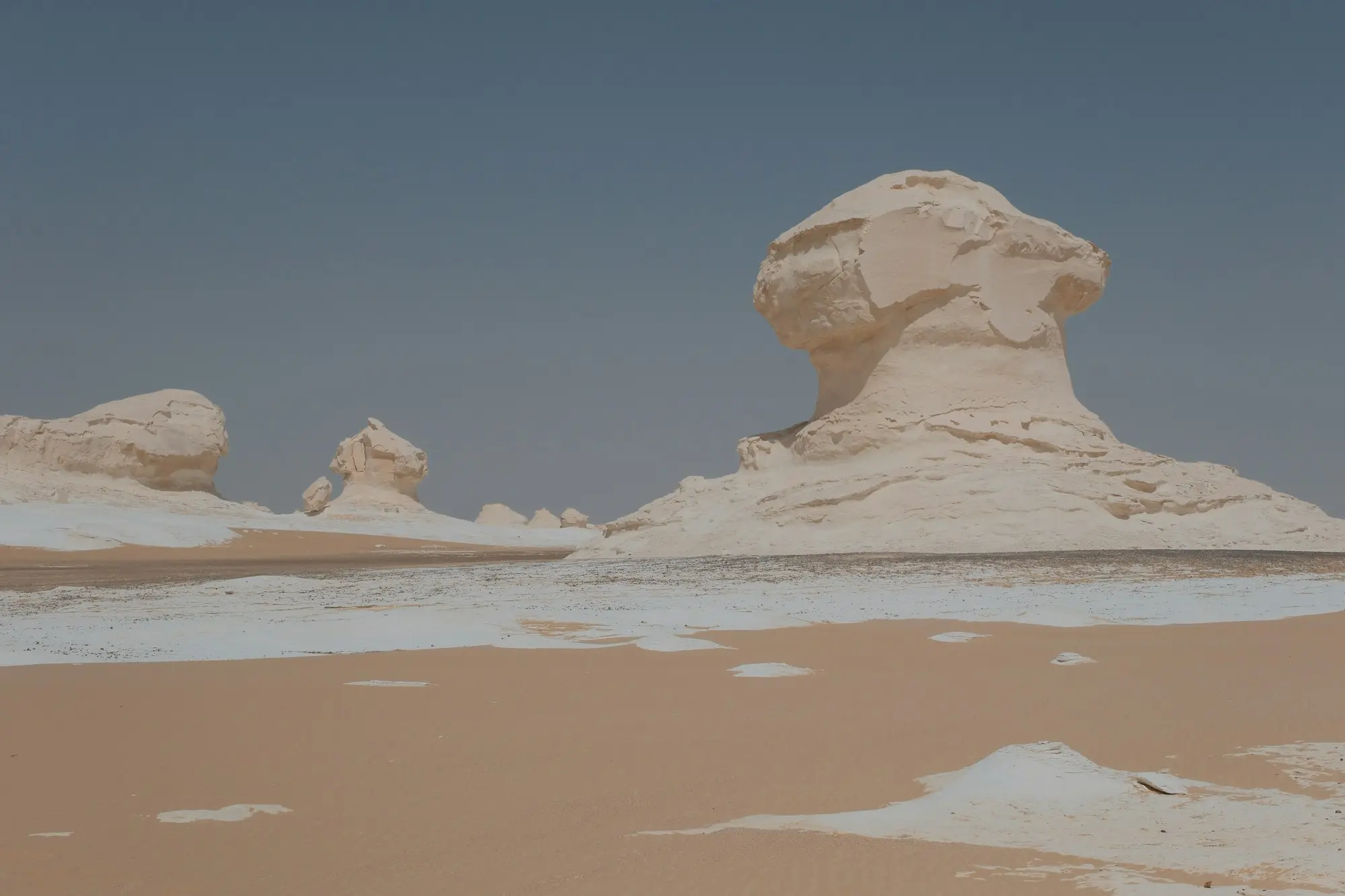 White chalk mushroom-shaped rock formations rising from sand and chalk patches under a slate-blue sky