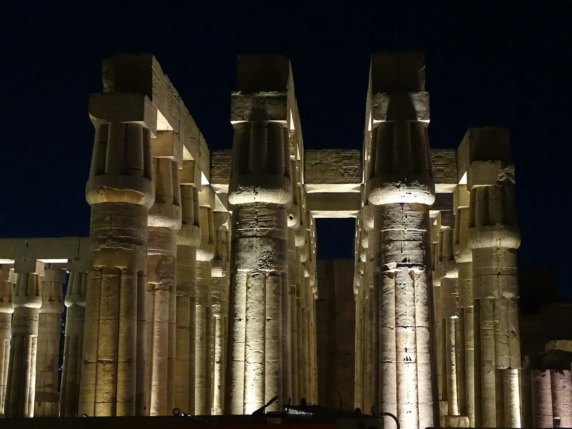 Floodlit papyrus-bundle columns of Luxor Temple glowing gold against a deep navy night sky