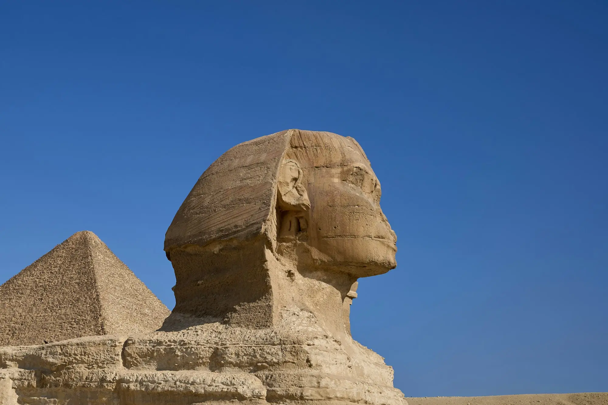 The Great Sphinx of Giza in profile against a deep blue sky, with the Great Pyramid behind it