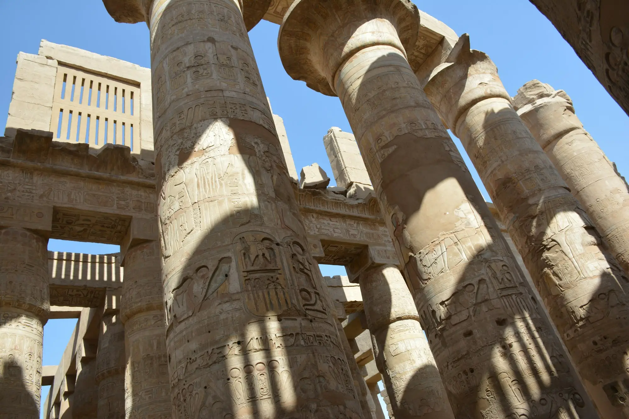 Carved hieroglyph columns of Karnak's Great Hypostyle Hall, striped with sunlight and shadow under a blue sky